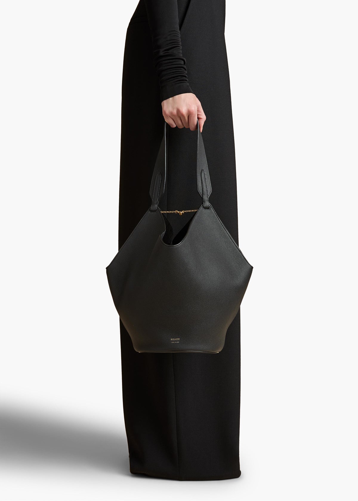 Structured black leather tote bag on a marble surface, architectural composition, dramatic side lighting